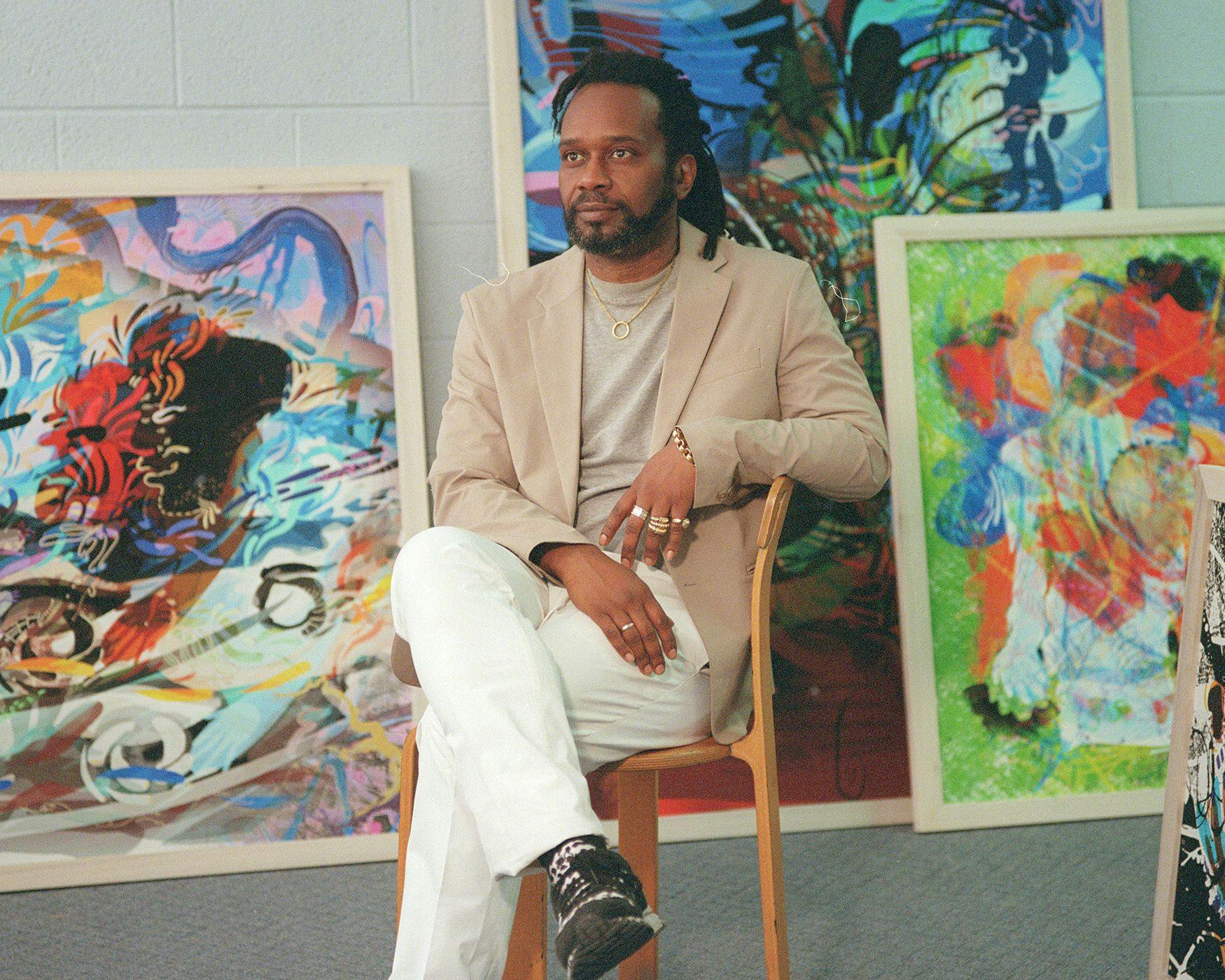 Moses Sun sits in a chair in his studio surrounded by paintings and books