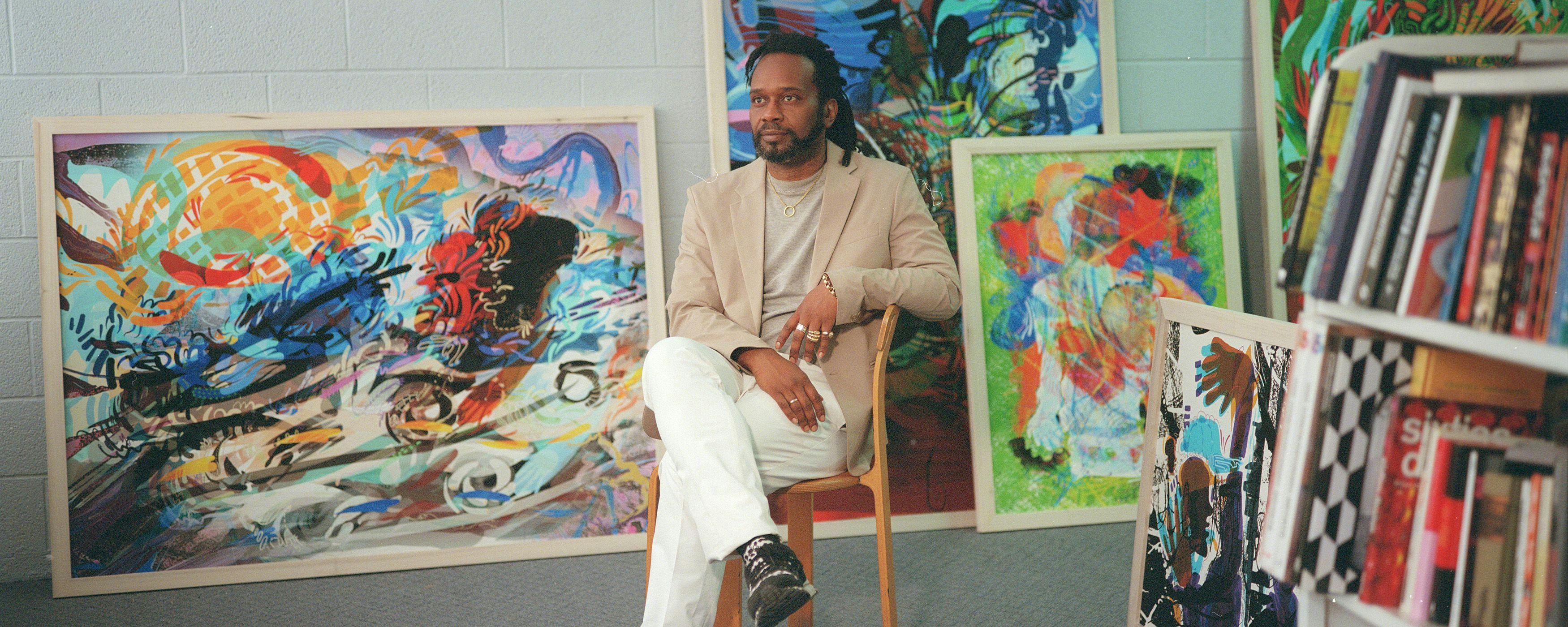 Moses Sun sits in a chair in his studio surrounded by paintings and books