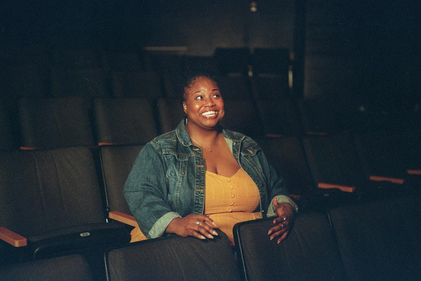 A woman sits alone in a theater, smiling broadly