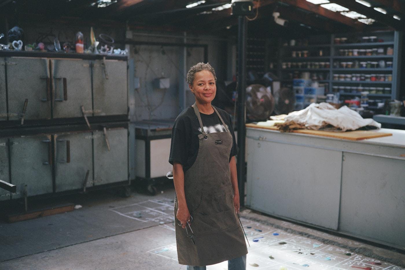 Deborah Moore stands in her studio/hot shop wearing a work apron