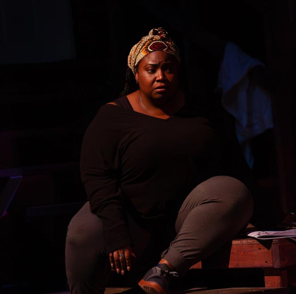 A woman sits on stage bathed in low light