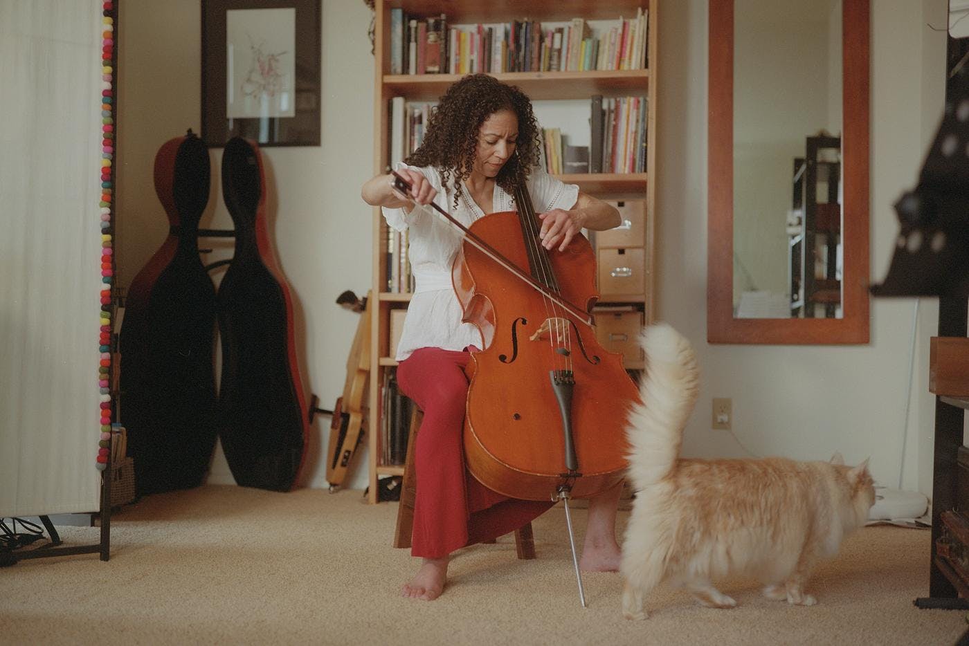 Gretchen Yanover plays her cello at home while a cat walks past her