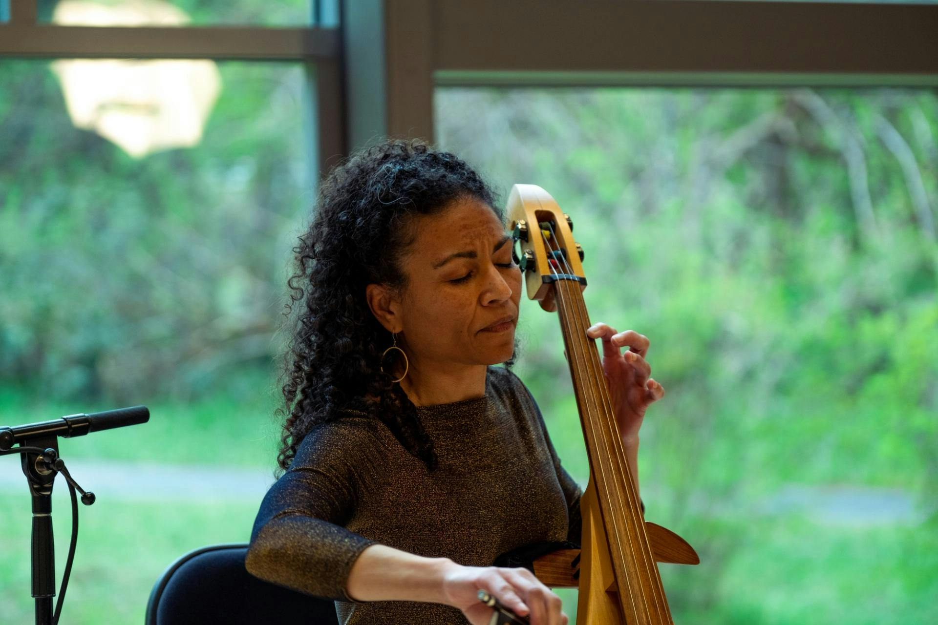 Gretchen Yanover plays her cello in front of a windows with greenery outside