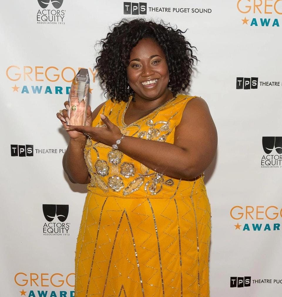 A woman in a long yellow dress holds a trophy