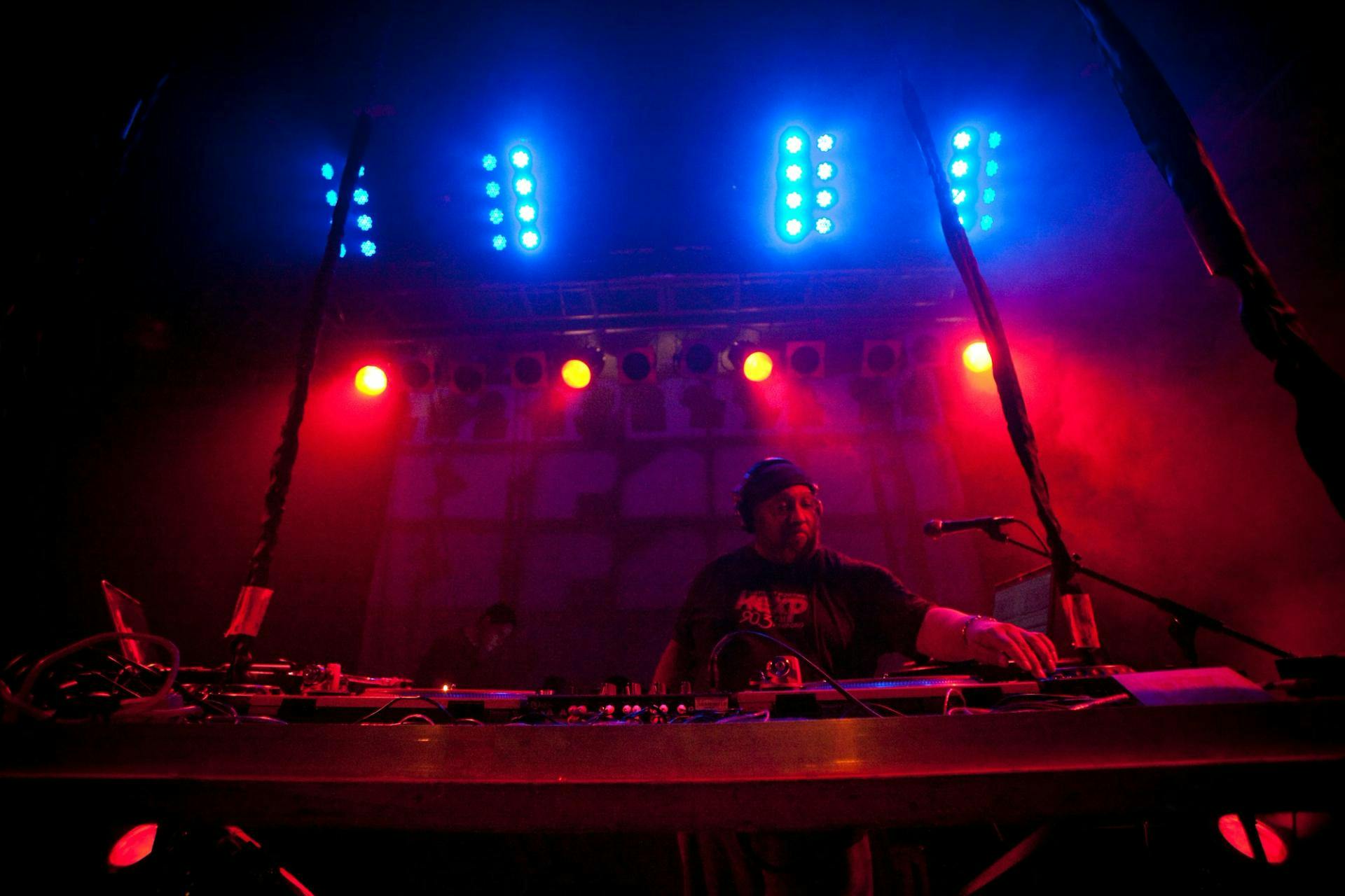 Riz Rollins in the DJ booth, bathed in red and blue light
