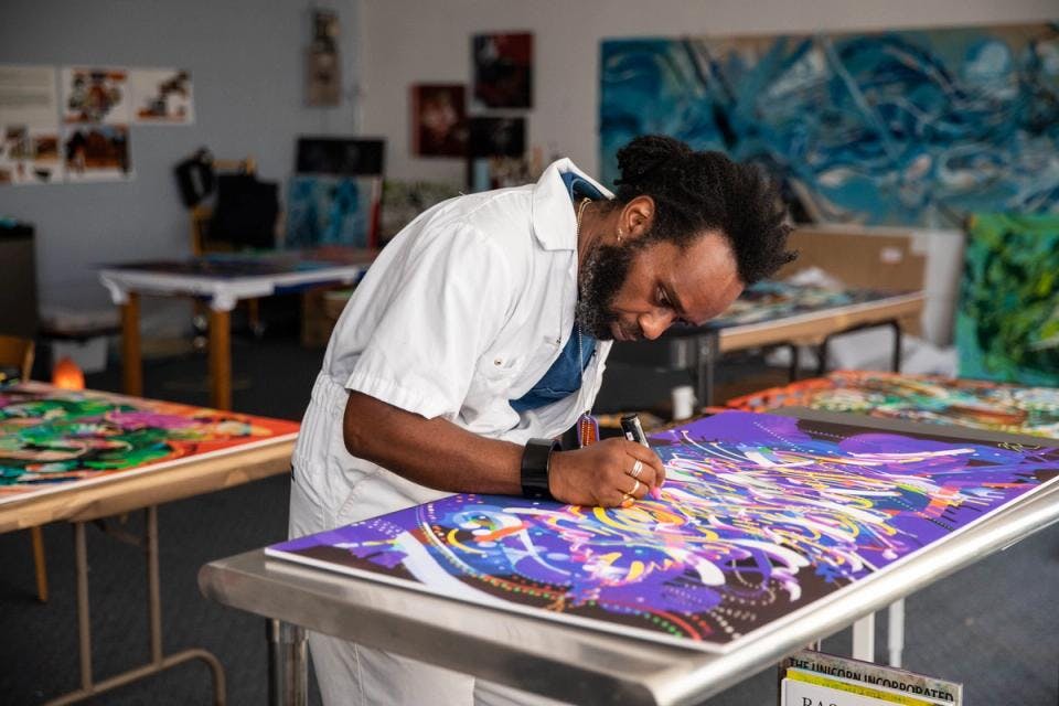 Moses Sun leans over a worktable to add detail to painting-in-progress