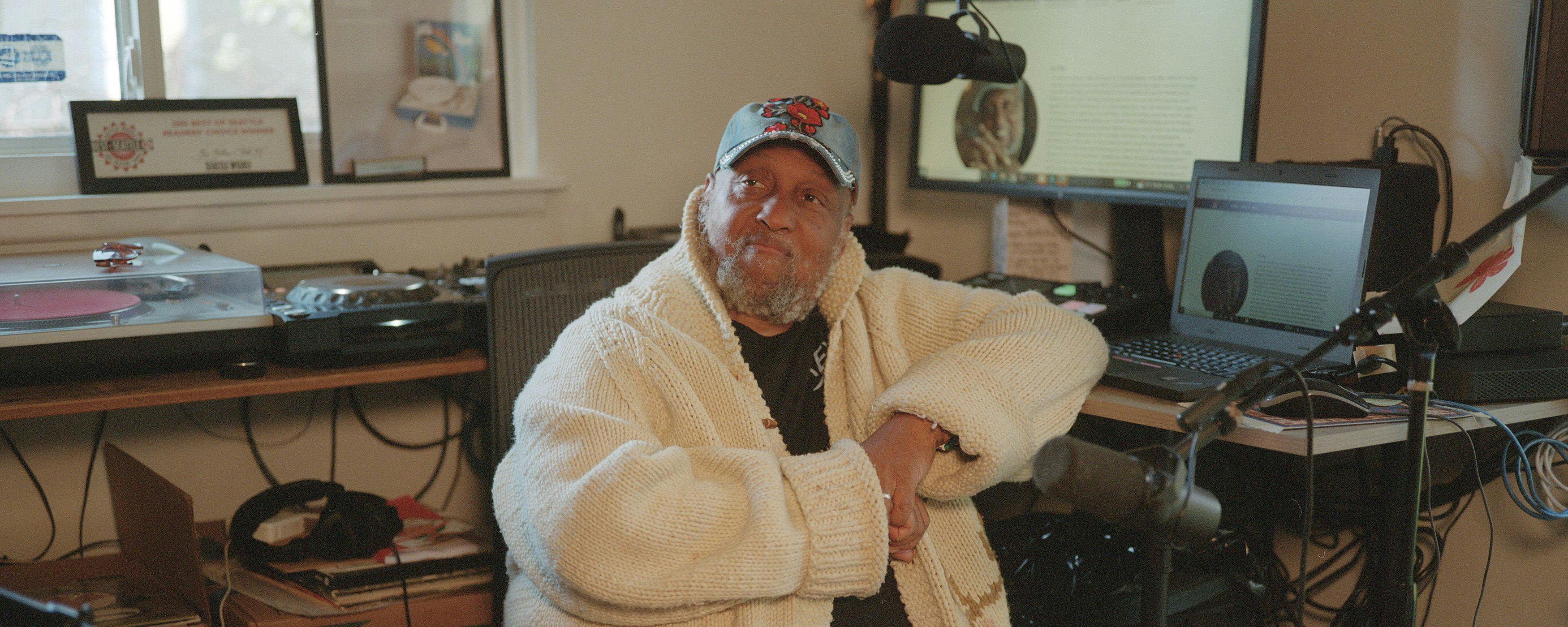 Riz Rollins in his home studio wearing a white cardigan and surrounded by gear
