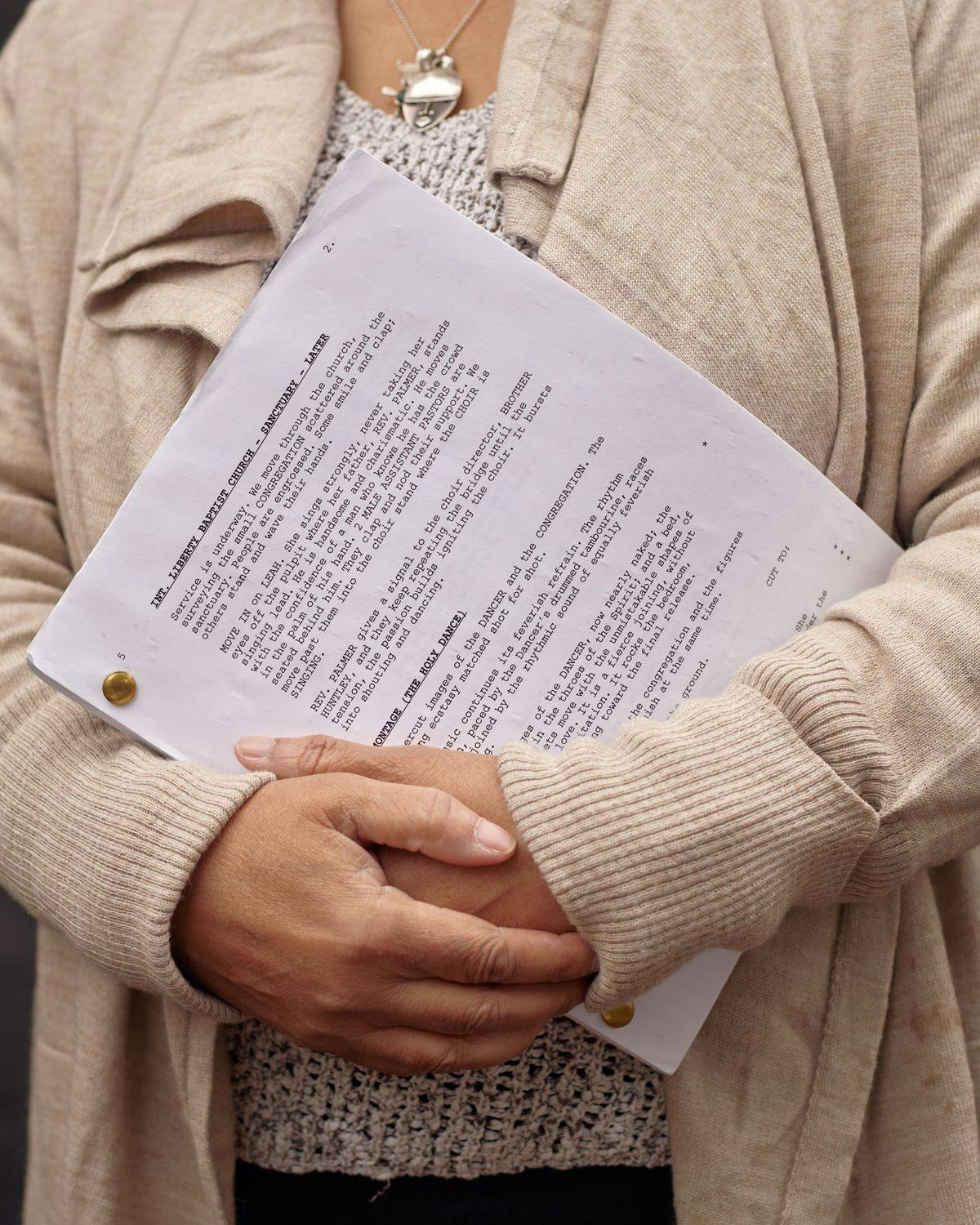Person in beige jacket holding a script, black letters on white printed paper face the viewer