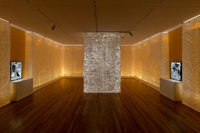 paper cut tyvek panels in a room, lit with a golden light from the back