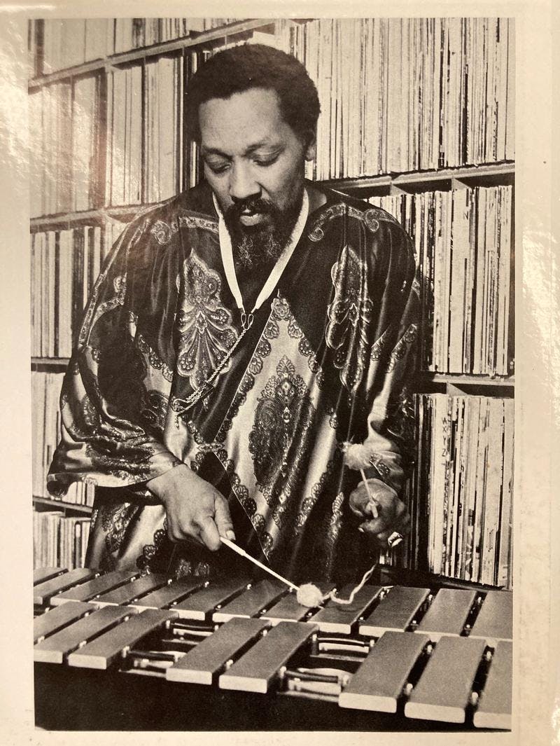 A black and white photo of a man playing the vibraphone in front of shelves of records