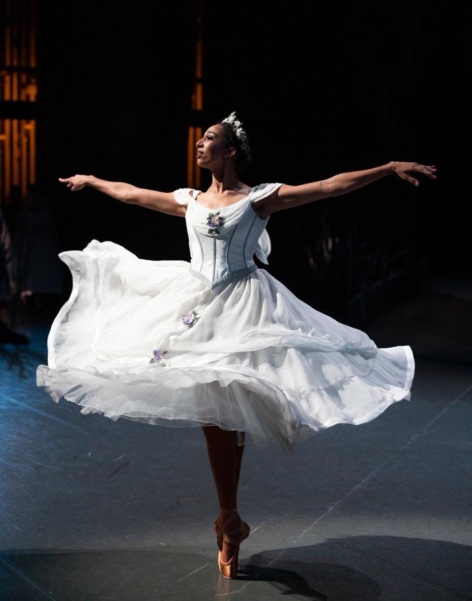 A ballerina on stage mid-spin, arms extended, wearing a white dress with full skirt
