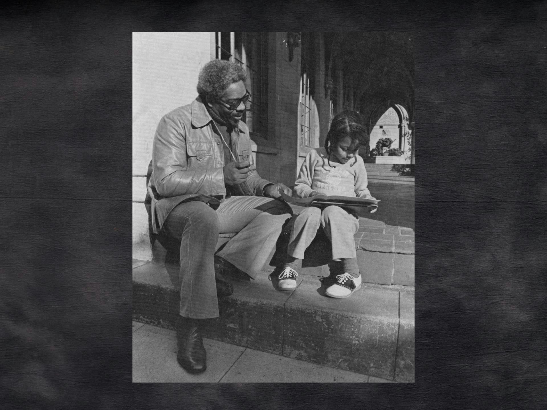 A black and white vintage photo of a man sitting with a girl on steps; he appears to be reading with her