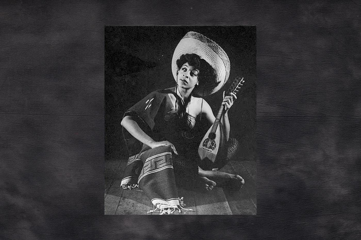 A black and white photo of a woman sitting down and holding a mandolin