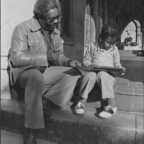 A man sits with a child, appearing to read a book with her 