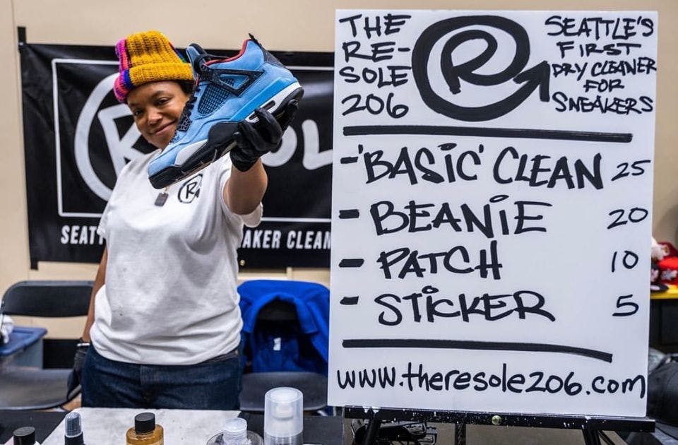 A woman holds a blue and white sneaker next to a whiteboard sign at a booth