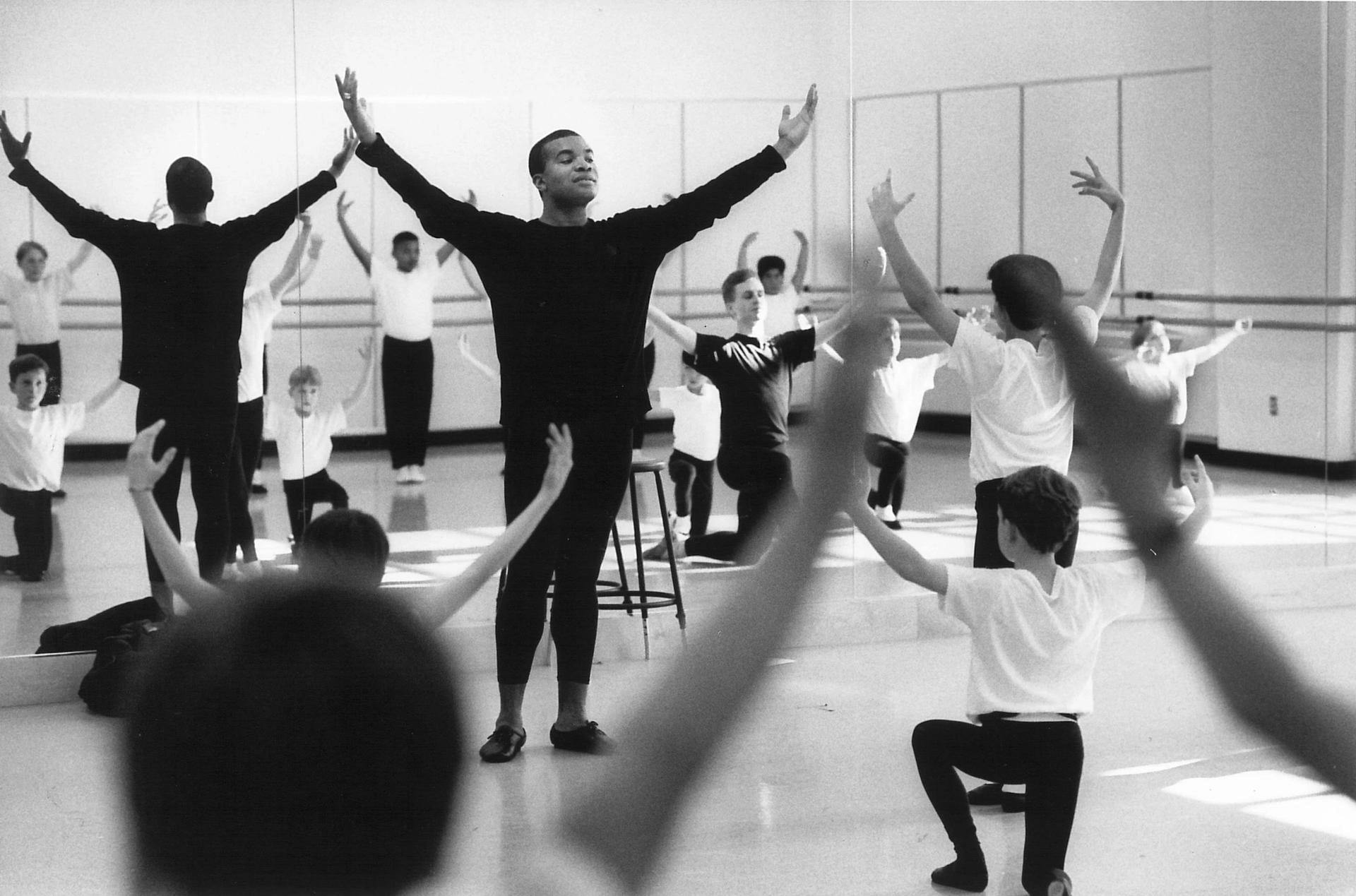 black and white photo of person with arms up in the air in dance rehearsal room
