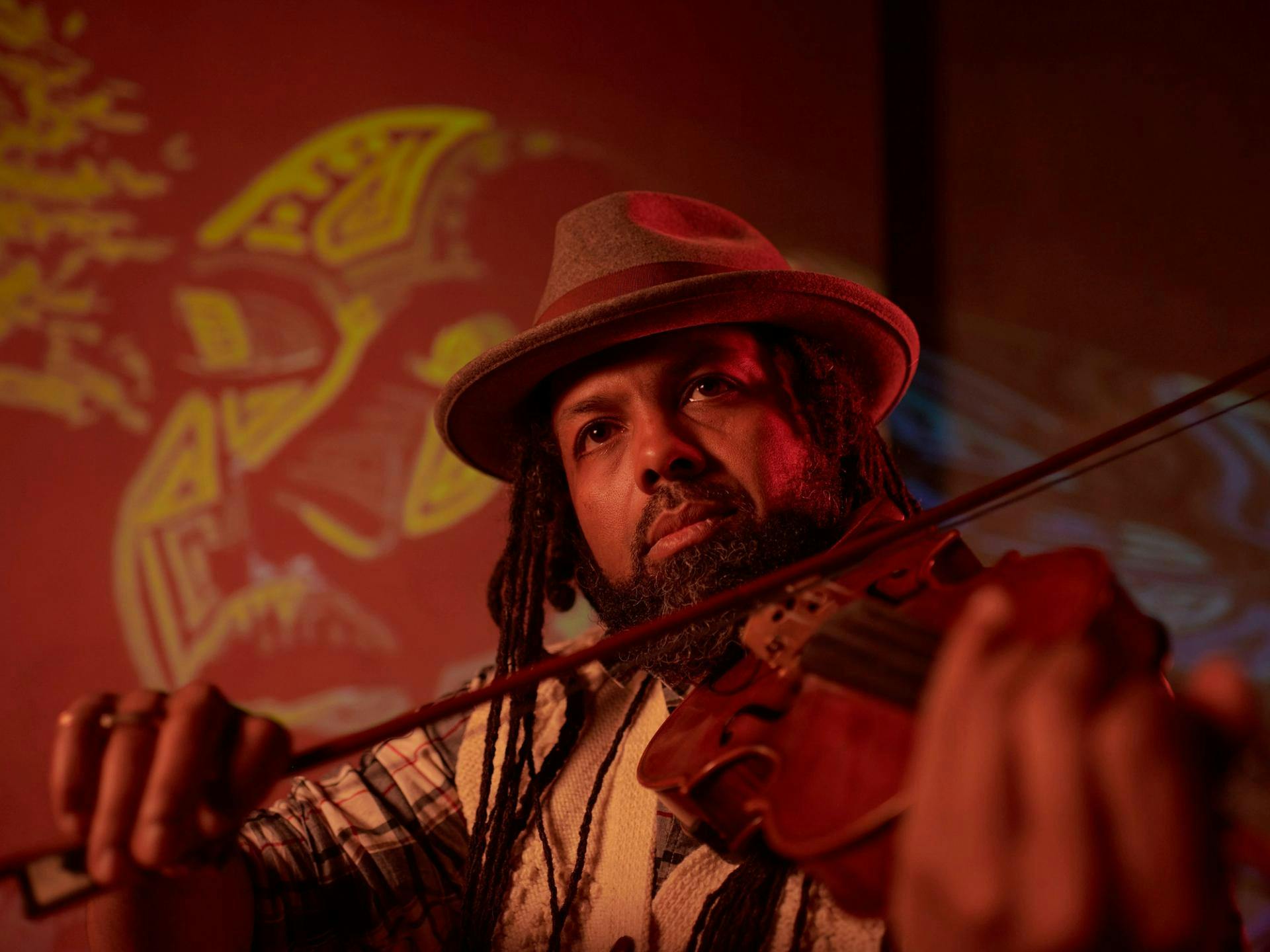 A man plays the violin while looking off in the distance with abstract projections behind him