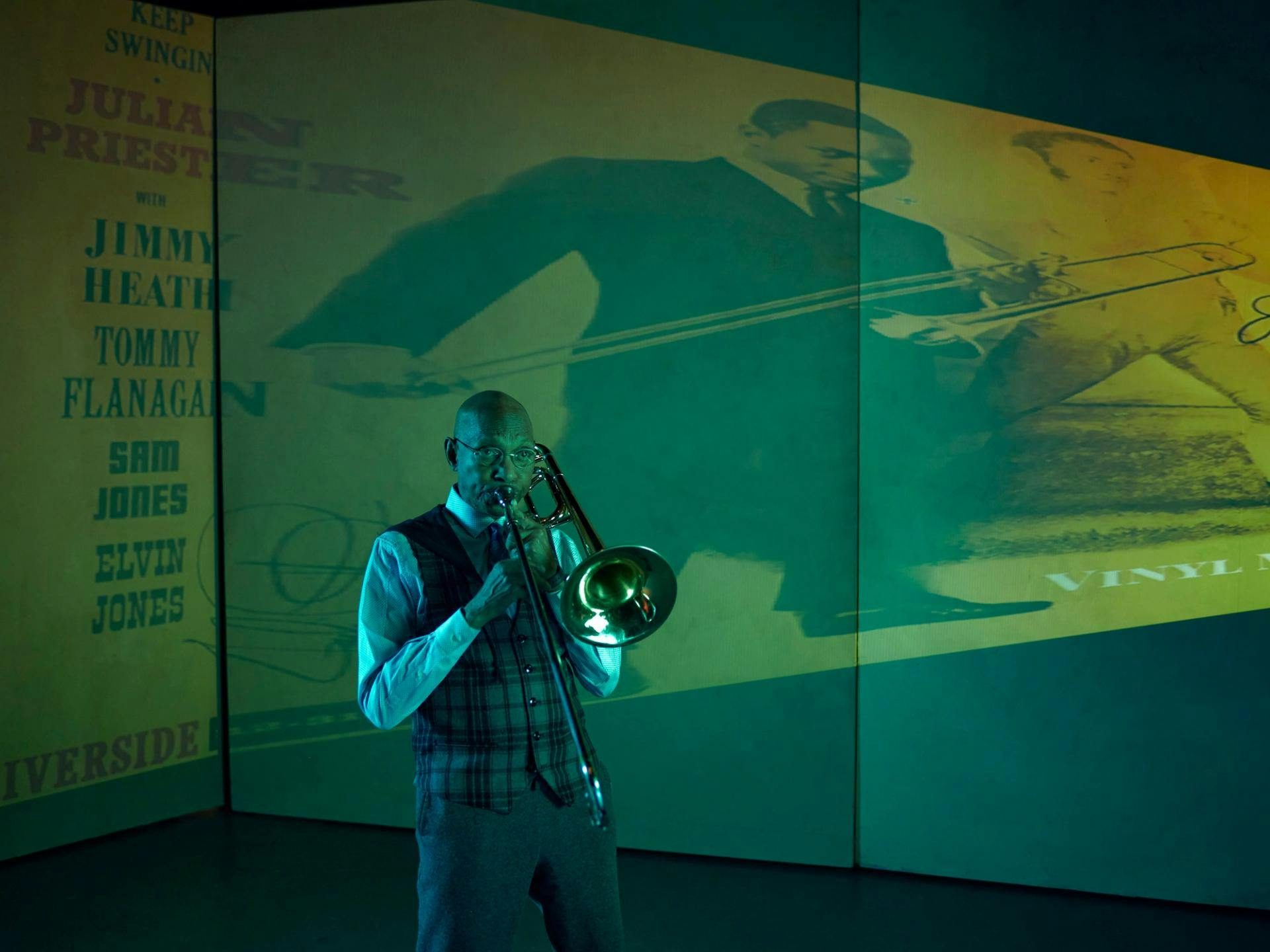 A man plays a trombone in front of a projection