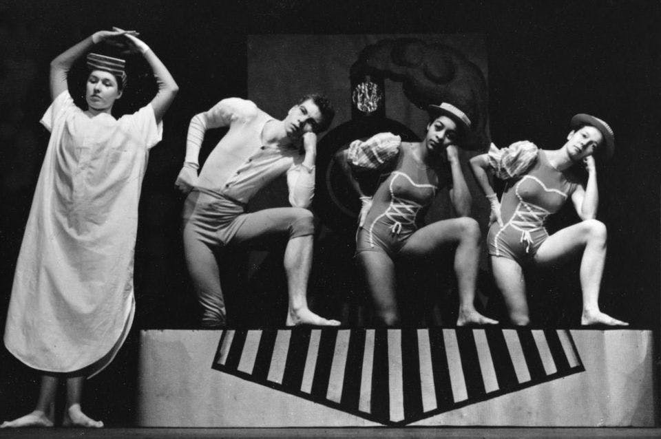 A black and white photo of people dancing on a stage in costumes