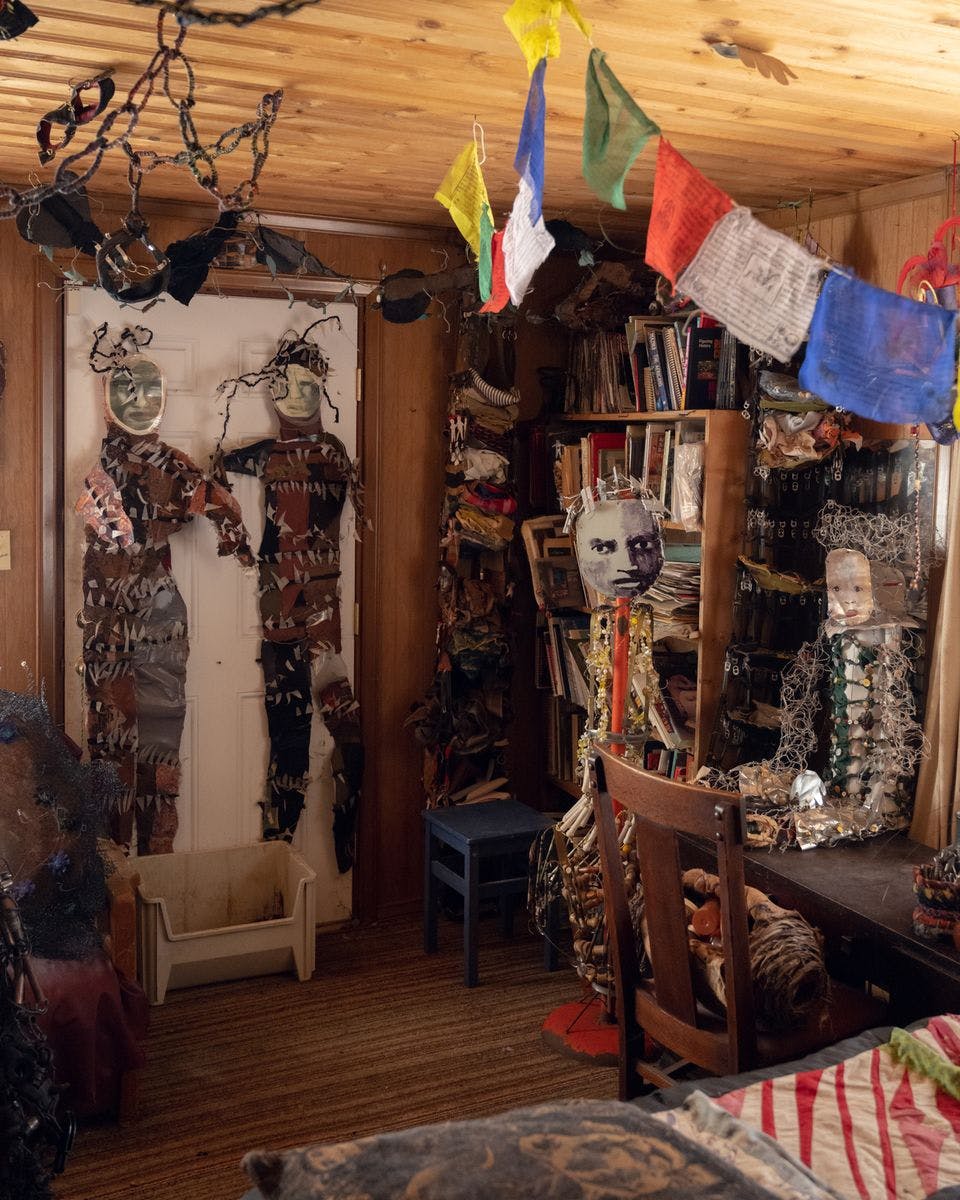 Inside of a studio; flags are hung, and there are several dolls strewn about or hanging on the wall