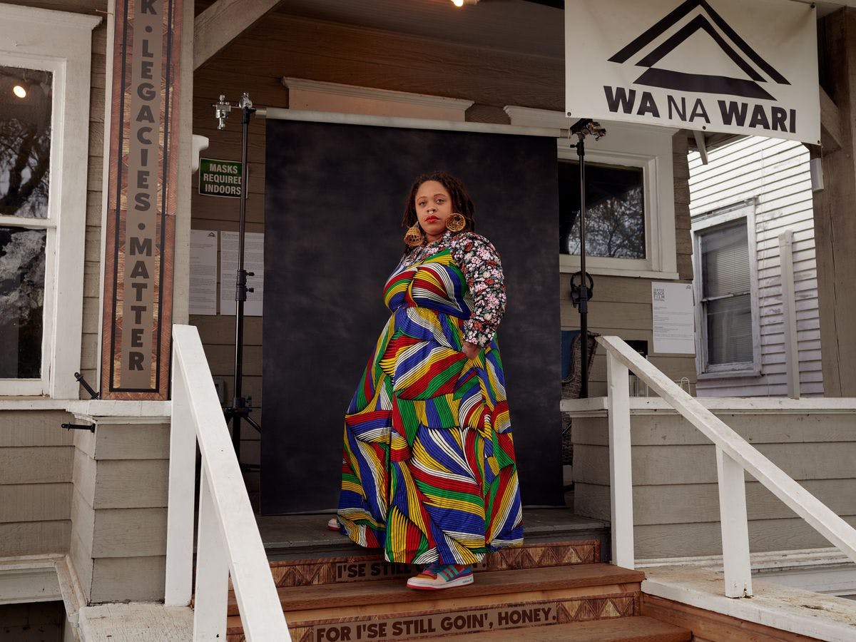 Person on stairs in a colorful dress, a banner hanging above says: Wa Na Wari 